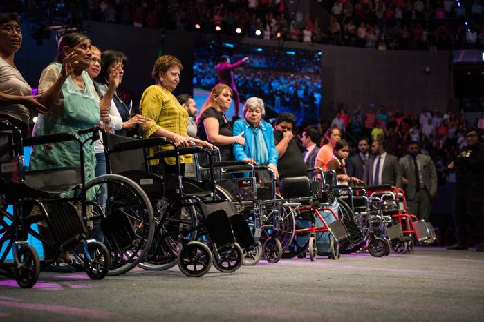 A row of empty wheelchairs with people standing behind them