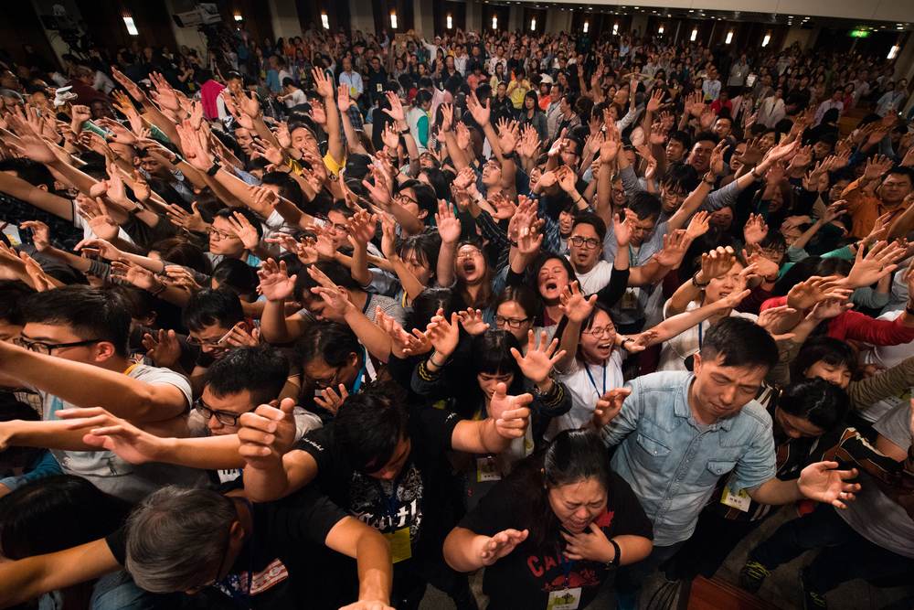 A packed hall with hands raised